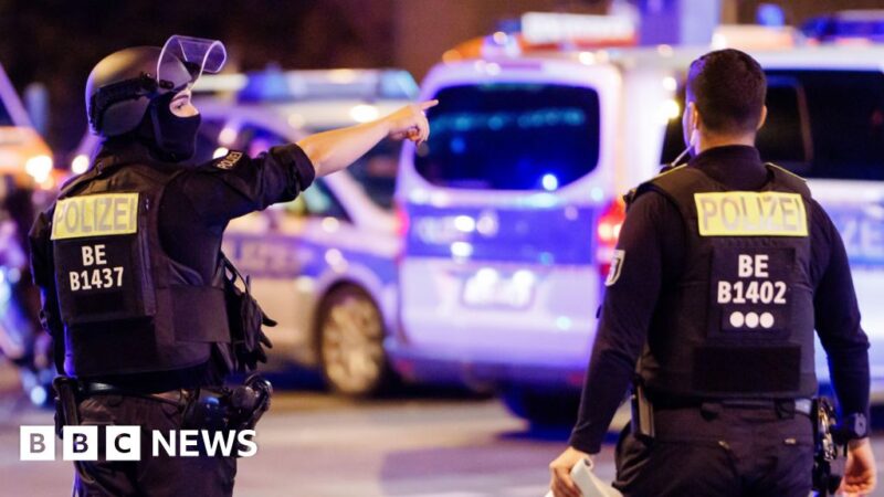 A police officer carrying a machine gun (L) and a colleague talk near the scene where several people were injured on the