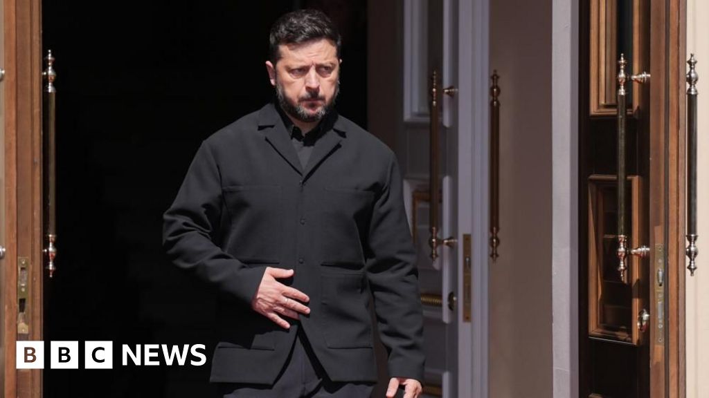 Zelensky, wearing a dark suit, walking through a doorway