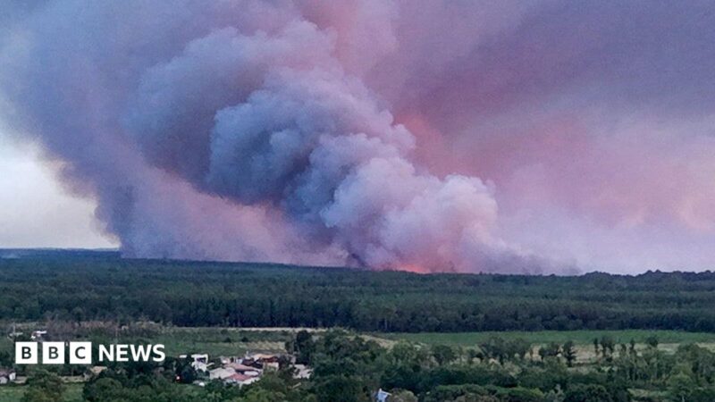 A drone view showing the Sainte-Helene commune in France with smoke rising in the background during a wildfire in a forest