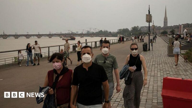 People wearing masks to protect themselves from smoke walk along the river in central Bordeaux. The sky is very hazy