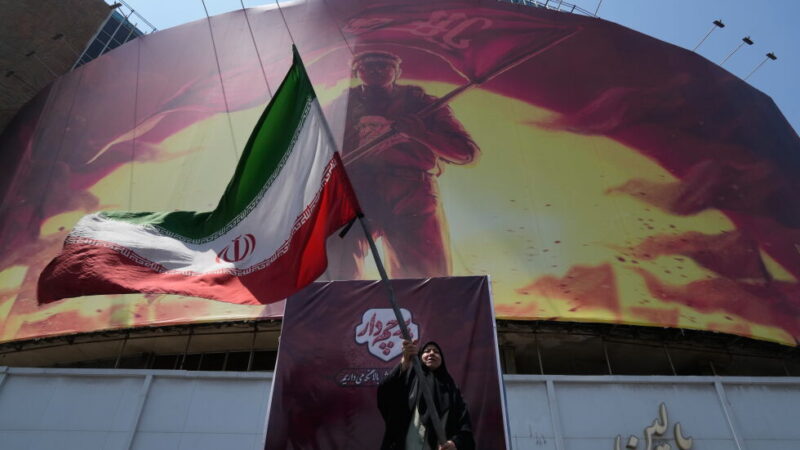 A woman waves an Iranina flag next to a billboard showing a graphic of a man wearing a shirt showing the face of late