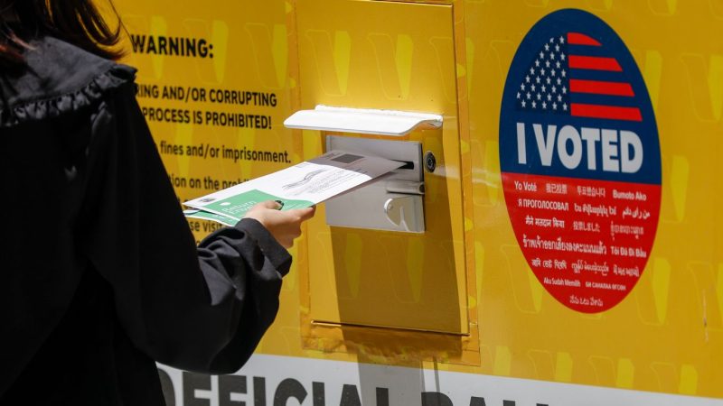 A person places their ballot inside a ballot box during early voting outside of the LA County Registrar-Recorder building on