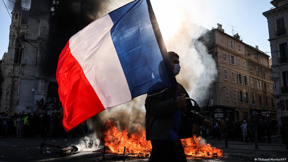 A protester waving a French national flag walks past a fire during clashes prior to the start of a demonstration to protest