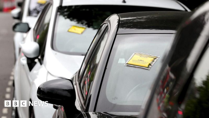 A generic-looking image shows a row of cars seen front-on with yellow and black Penalty Charge Notices affixed to their