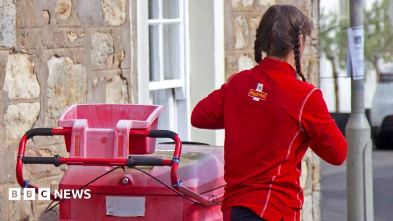 A postwoman seen from behind, wearing a Royal Mail top and standing beside a mail trolley on a residential road