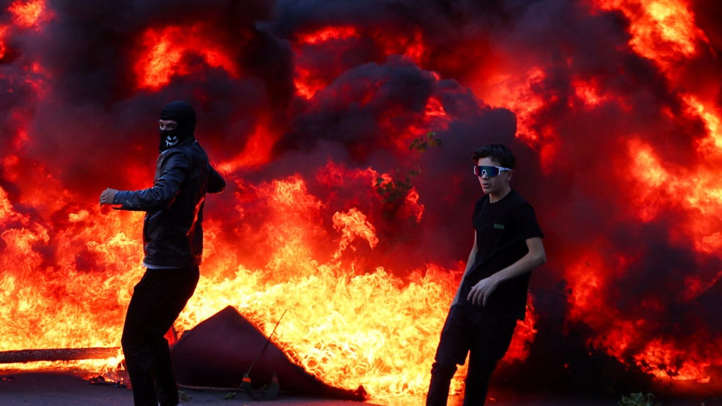 People react near a burning fire as plumes of black smoke rise amid an anti-government protest by students in Tirana