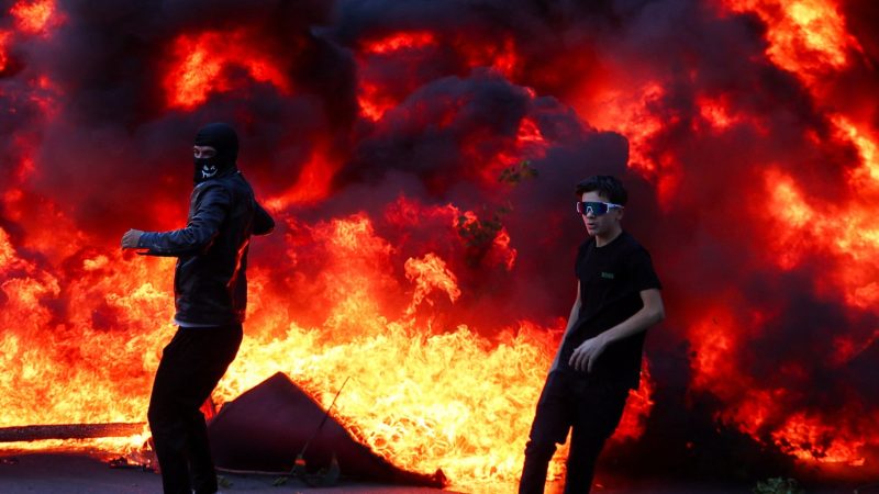 People react near a burning fire as plumes of black smoke rise amid an anti-government protest by students in Tirana