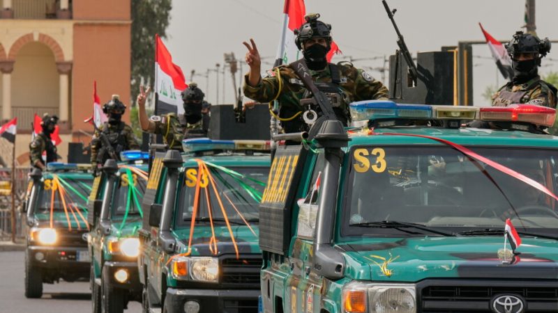 Iraqi security officers flash victory signs as they ride on vehicles decorated with national flags and ribbons during a