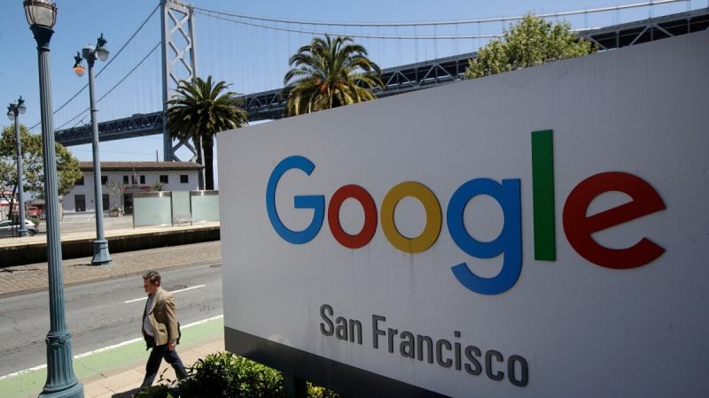 In this May 1, 2019, file photo a man walks past a Google sign outside with a span of the Bay Bridge at rear in San
