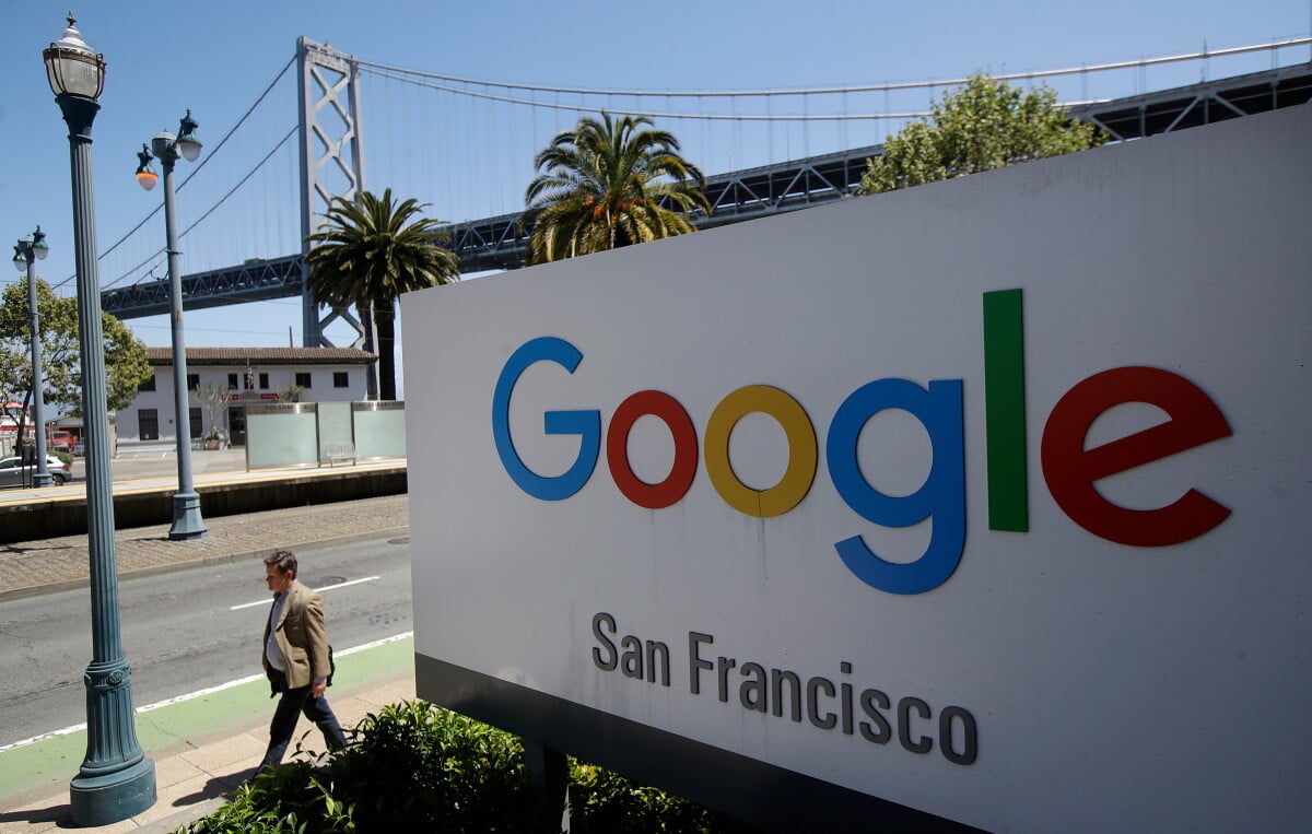 In this May 1, 2019, file photo a man walks past a Google sign outside with a span of the Bay Bridge at rear in San