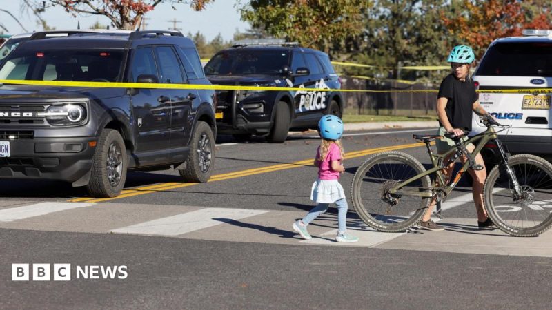 A girl and woman cross the road with police cars and tape in the background