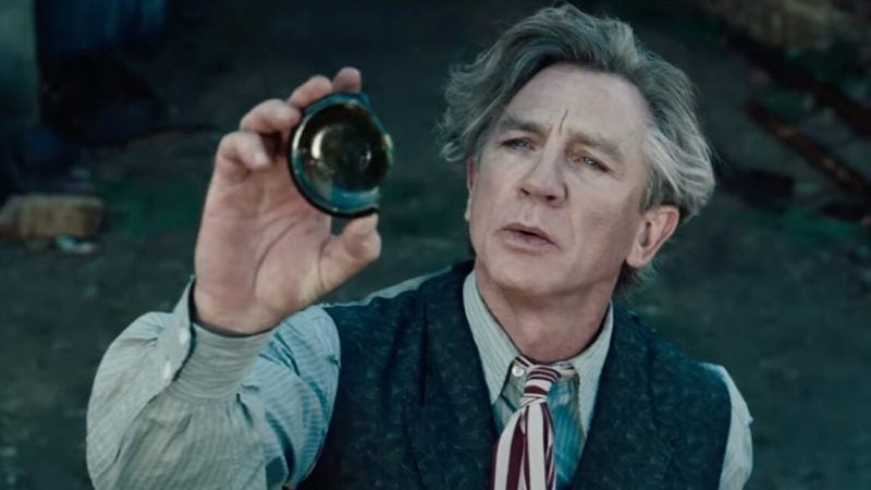 Middle aged man with wild gray hair in 1950s clothes holding up the broken off bottom of a green glass bottle